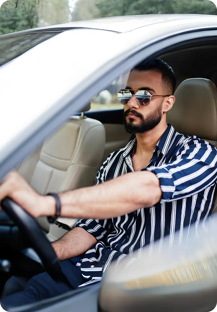 A woman in a navy hijab sits in a car, holding a phone to her ear. She looks thoughtful, gazing outside. The interior is neutral-toned, creating a calm mood.
